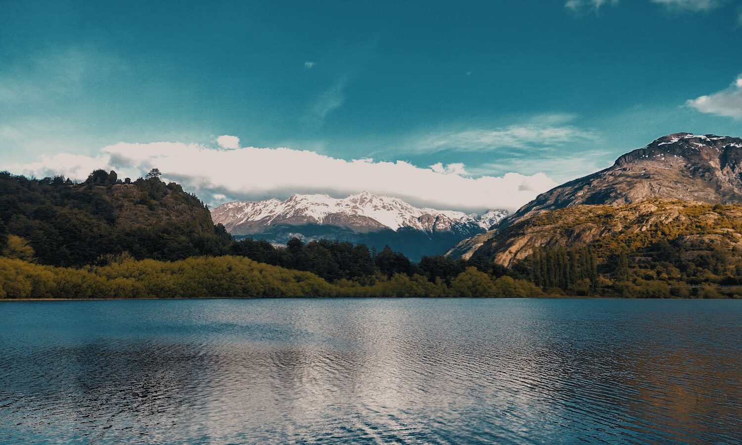 Calm lake with snow-capped mountains and lush greenery in Futaleufú, Chile.