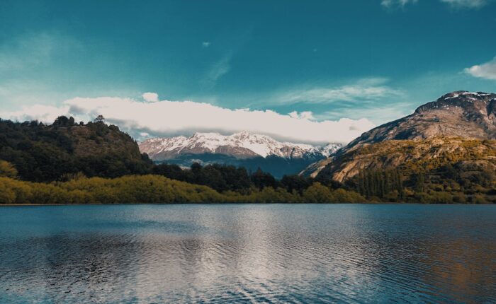 Calm lake with snow-capped mountains and lush greenery in Futaleufú, Chile.