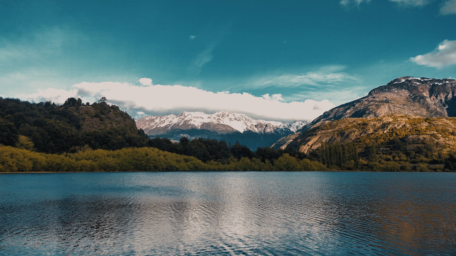 Calm lake with snow-capped mountains and lush greenery in Futaleufú, Chile.