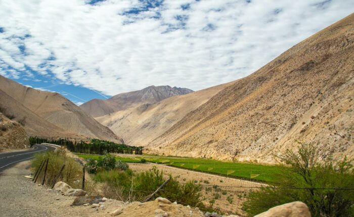 Breathtaking valley in Pisco Elqui, Chile with brown mountains and green fields under a cloud-dappled sky.