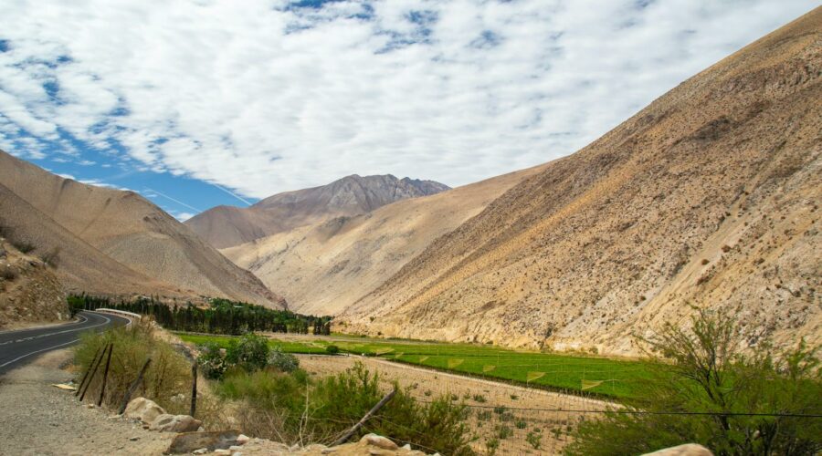 Breathtaking valley in Pisco Elqui, Chile with brown mountains and green fields under a cloud-dappled sky.