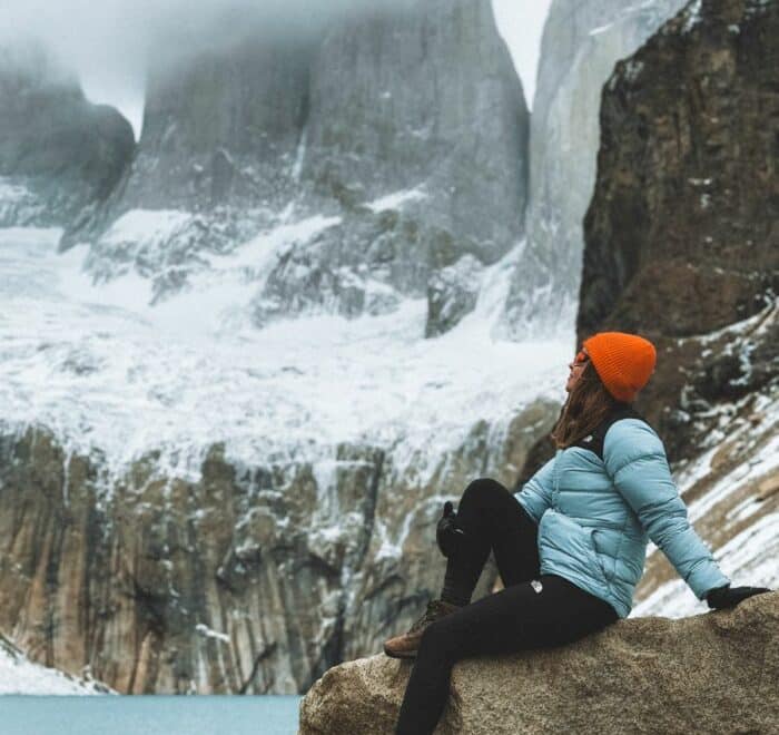 Person sitting on a rock in Torres del Paine, Chile, admiring snowy peaks.